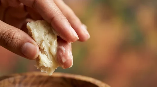 Texture onctueuse de beurre de karité brut entre des mains protectrices