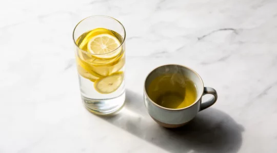 Composition minimaliste avec verre d'eau citronnée et tasse de thé vert sur surface blanche