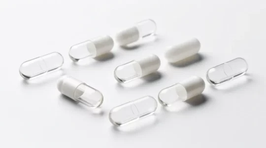 Gélules de compléments alimentaires avec comparaison des matériaux végétaux et effet de transparence sur fond blanc épuré